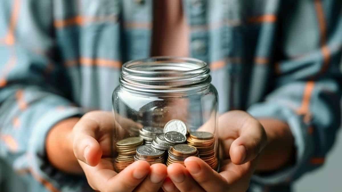 Finanzielle Kontrolle live below your means by saving spare coins in a glass jar held with both hands, symbolizing mindful budgeting and everyday financial discipline