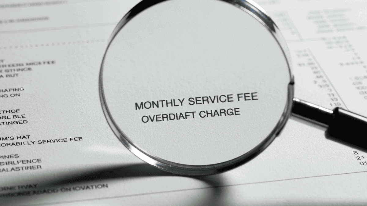 A close-up, detailed shot of a magnifying glass hovering over the "fine print" of a bank statement, highlighting hidden fees like "maintenance" or "overdraft."