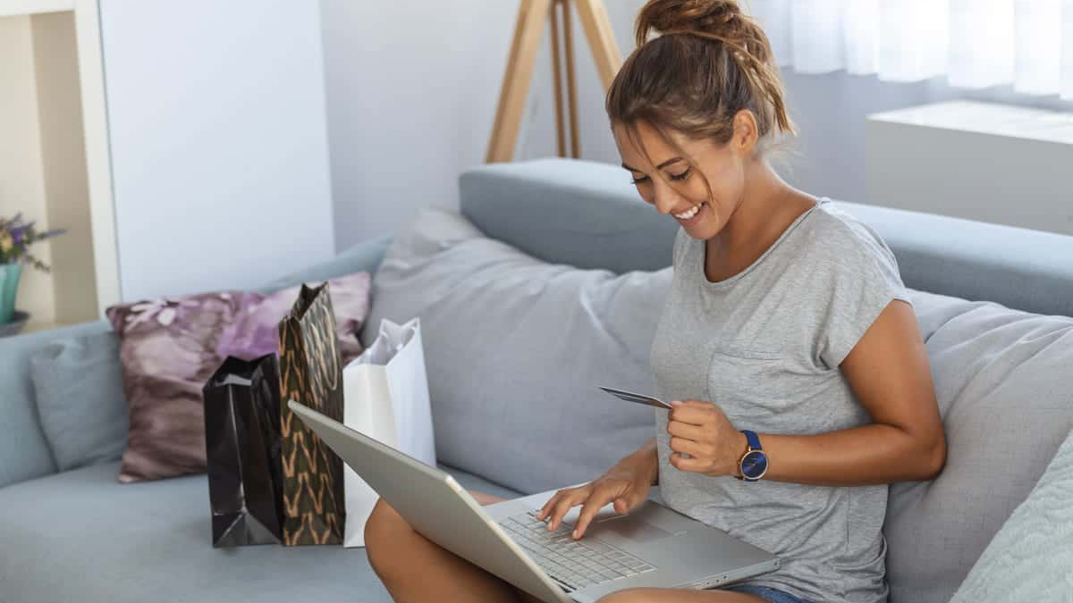 Einkaufen The image shows a young woman comfortably seated on a sofa, happily engaged in online shopping using a laptop and a credit card.
