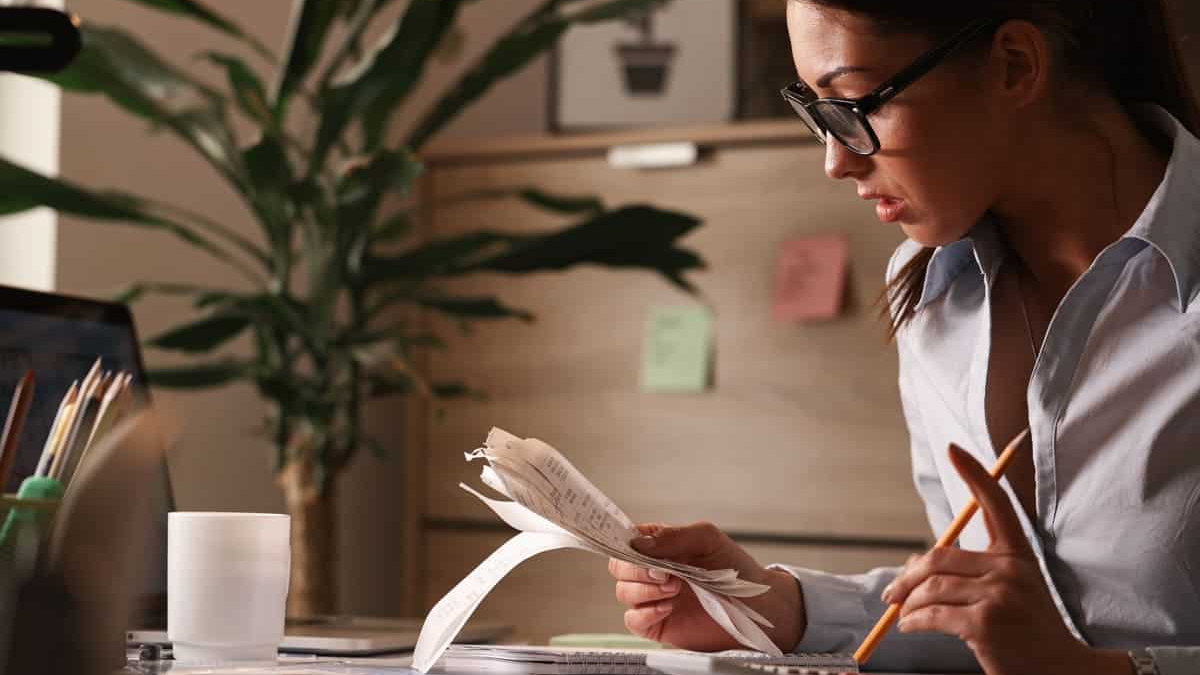 Finanzen The image shows a woman with dark hair and glasses working intently at a desk, seemingly managing finances or reviewing documents.