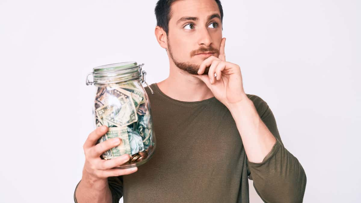 Geld financial confidence represented by a thoughtful young man holding a glass jar filled with cash, symbolizing careful planning, saving habits, and mindful money decisions