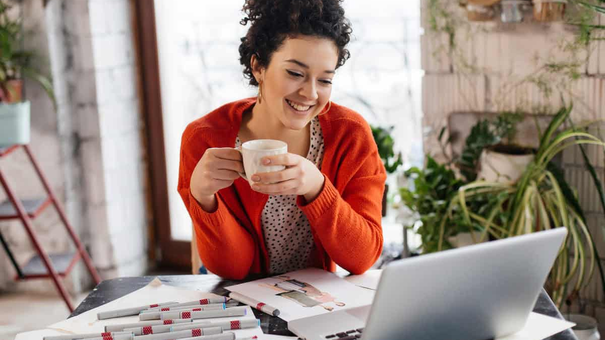Investment Paths for beginners can be explored from home, as shown by a woman reviewing notes and using a laptop while enjoying a cup of coffee.