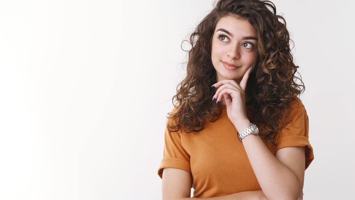 The image is a studio portrait of a young woman with curly brown hair, posed thoughtfully against a plain white background.