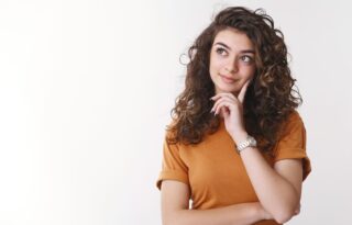 The image is a studio portrait of a young woman with curly brown hair, posed thoughtfully against a plain white background.