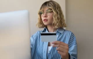 The image is a close-up of a young woman intently looking at a laptop screen while holding a credit card.