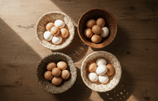 Overhead view of four woven baskets on a wooden table, each containing a few eggs, visually representing the diversification principle of not putting all eggs in one basket.