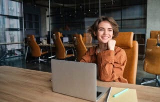 career roadmap professional smiling while working on a laptop at a modern office desk, planning long-term career and income growth