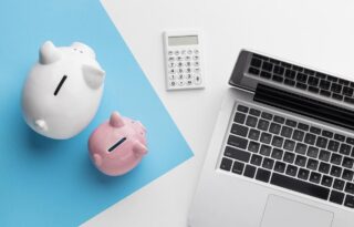 Two piggy banks beside a calculator and an open laptop, representing personal budgeting and financial cushion.