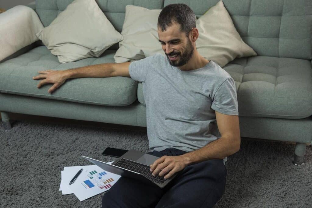 Financial cushion planning as a man sits on the floor with his laptop and printed charts, reviewing his personal budget at home.