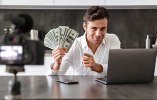 Earning potential illustrated by a man holding U.S. dollar bills while working on a laptop and recording content with a camera, suggesting online income growth and monetization strategies