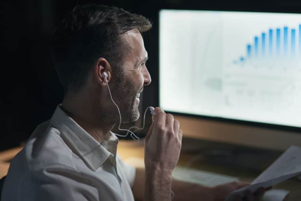 investing research at a home office with a man wearing earphones analyzing market charts on a desktop computer