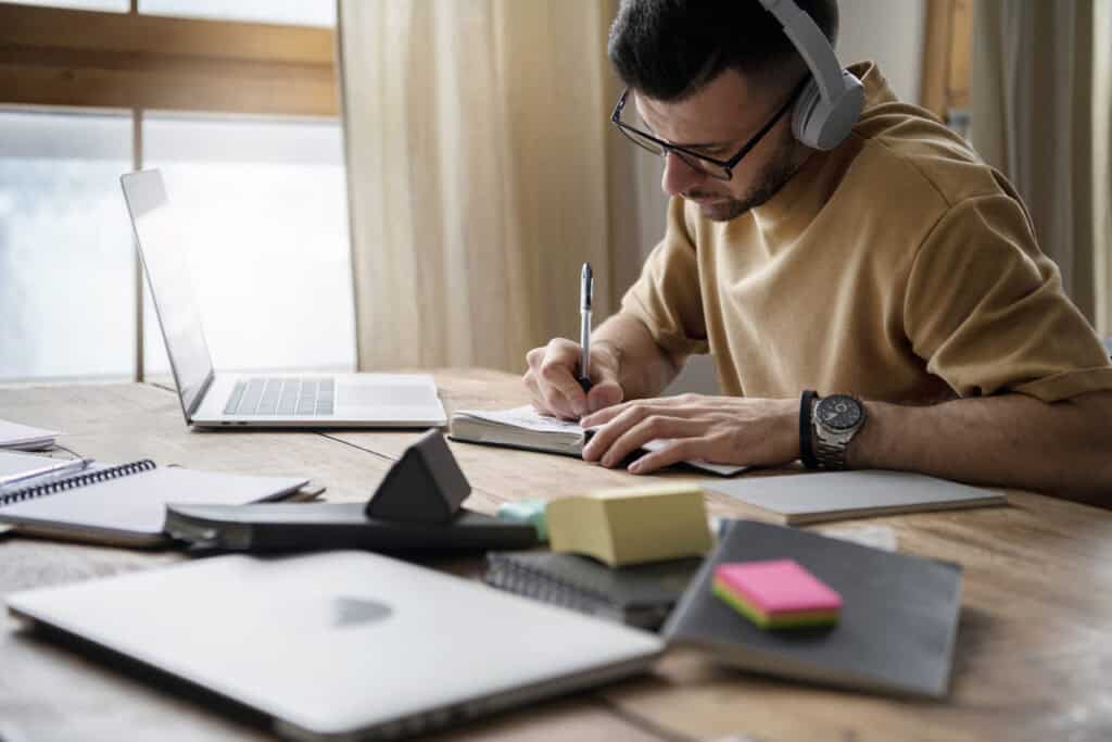 Investment Paths research in progress, showing a man wearing headphones taking notes while studying financial materials on his laptop.