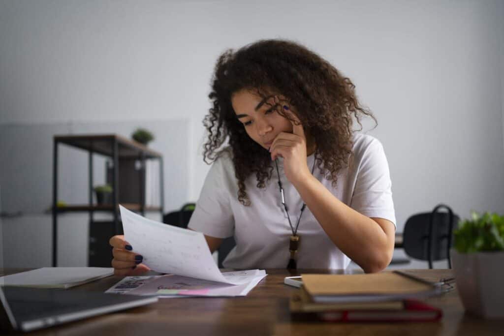 Smart cash flow strategies shown through a young woman reviewing bills and financial documents at a desk, analyzing expenses and planning personal finances.