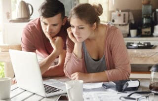 checking vs savings account comparison illustrated by a couple reviewing household finances on a laptop while a child looks on at the kitchen table